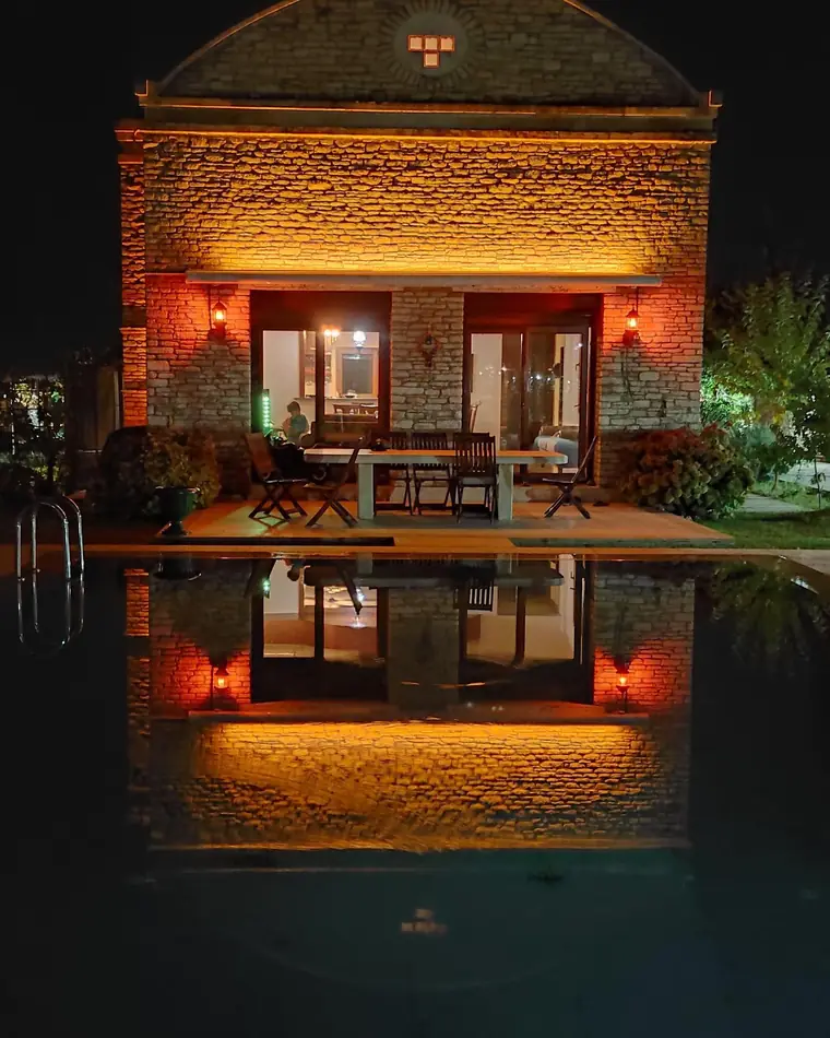 Gece aydınlatmalı taş ev ve havuzdaki yansıması